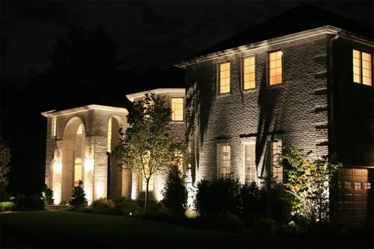 Elegant two-story home illuminated at night with soft landscape lighting, emphasizing architectural features and surrounding greenery.