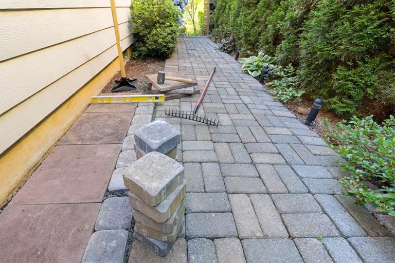 A newly installed hardscape pathway with tools like a rake, level, and stacked bricks, showcasing hardscape installation in progress and its challenges with soil erosion.
