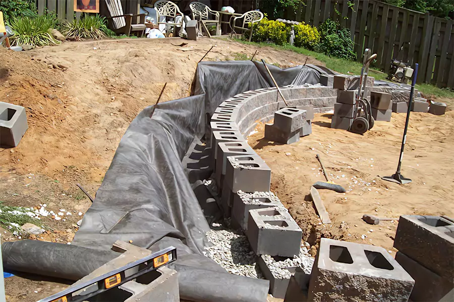 Retaining wall construction using durable materials for hardscape installation in Houston, TX, showing a curved block structure, gravel foundation, and landscape fabric for erosion prevention.