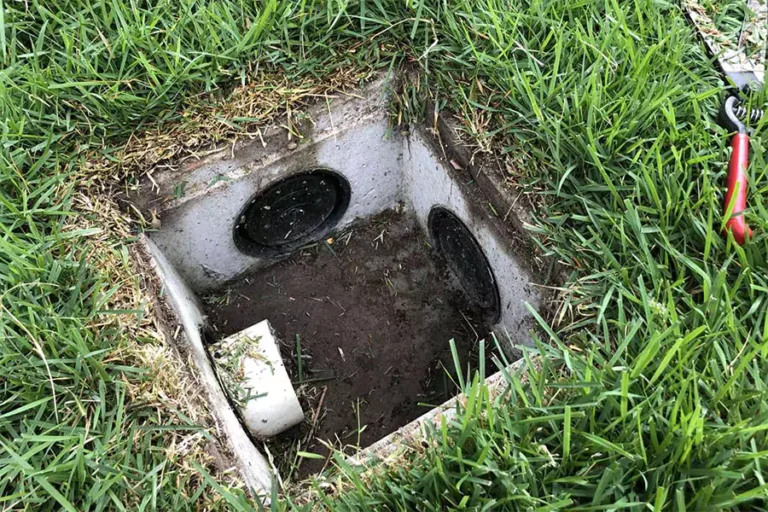 Open drainage inspection box in residential lawn showing potential blockage issues, crucial for homeowners to identify early signs of drainage problems