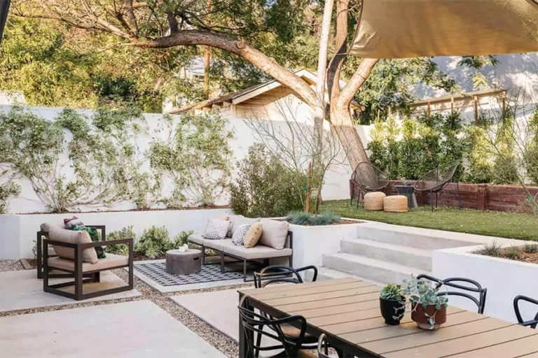 Modern backyard landscaping in Houston TX with outdoor furniture, tiered patio design, shade sail, and low-maintenance plants