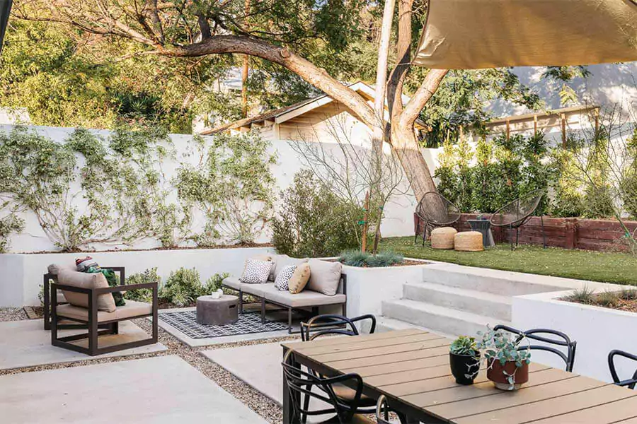 Modern backyard landscaping in Houston TX with outdoor furniture, tiered patio design, shade sail, and low-maintenance plants