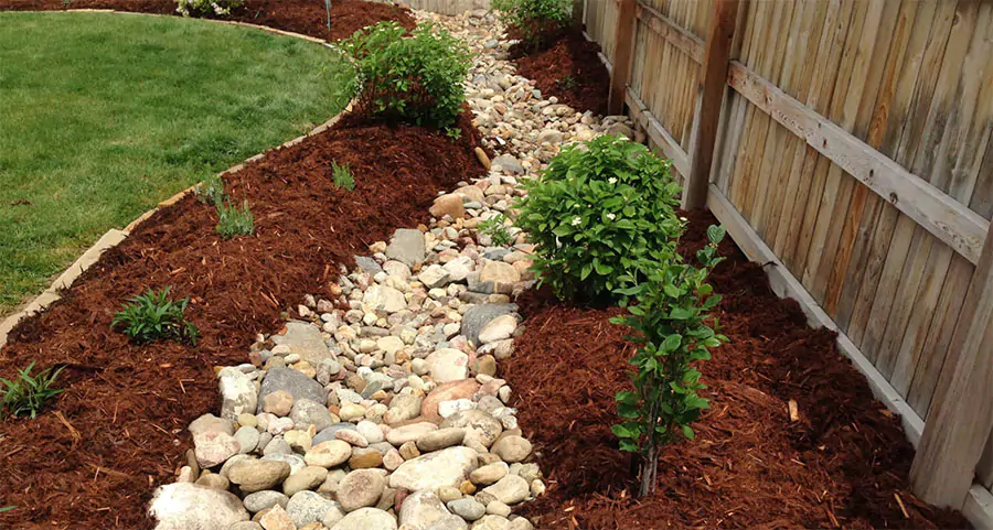 Dry creek bed with decorative rocks and mulch used for backyard drainage and erosion control in Houston landscaping