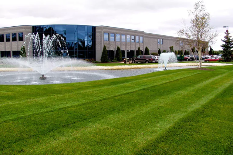 Well-maintained commercial landscaping in Cypress, TX featuring a lush green lawn, water fountain, and modern office building, showcasing the environmental benefits of professional landscape design and care.