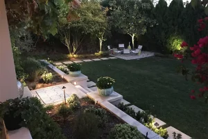 Backyard landscape design with outdoor lighting, stone pathways, garden planters, and seating area in Cypress TX home