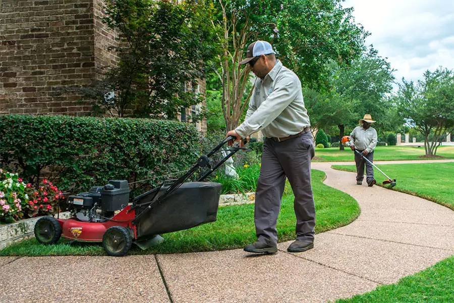 Two professional lawn care workers mowing and trimming a residential yard in Cypress, TX, showcasing expert landscaping and grass maintenance services.